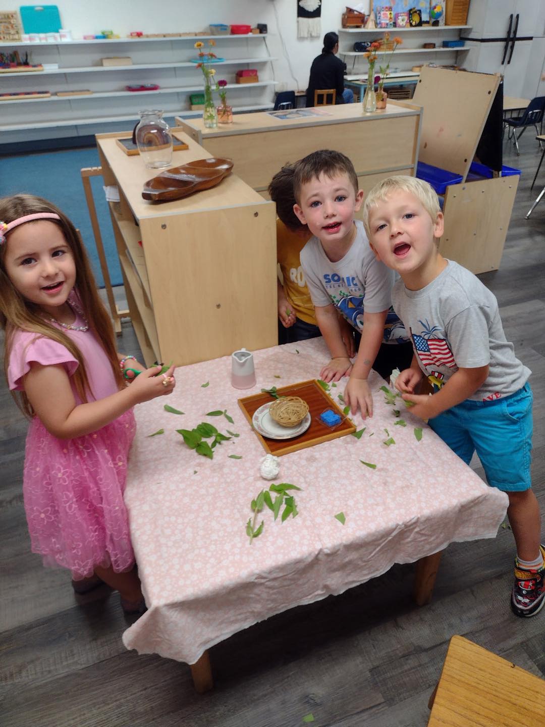Three preschoolers snipping leaves at a cloth-covered table