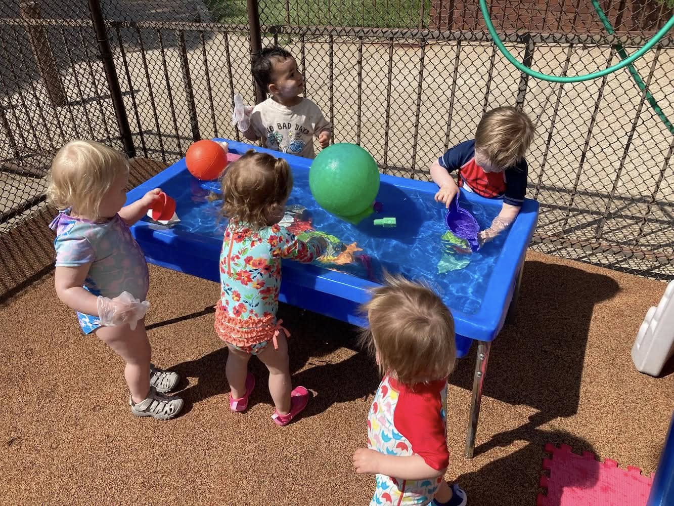 Four toddlers playing together around a blue water table outside