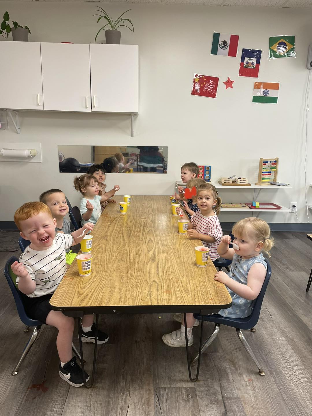 Toddlers seated along a classroom table eating cups of shaved ice