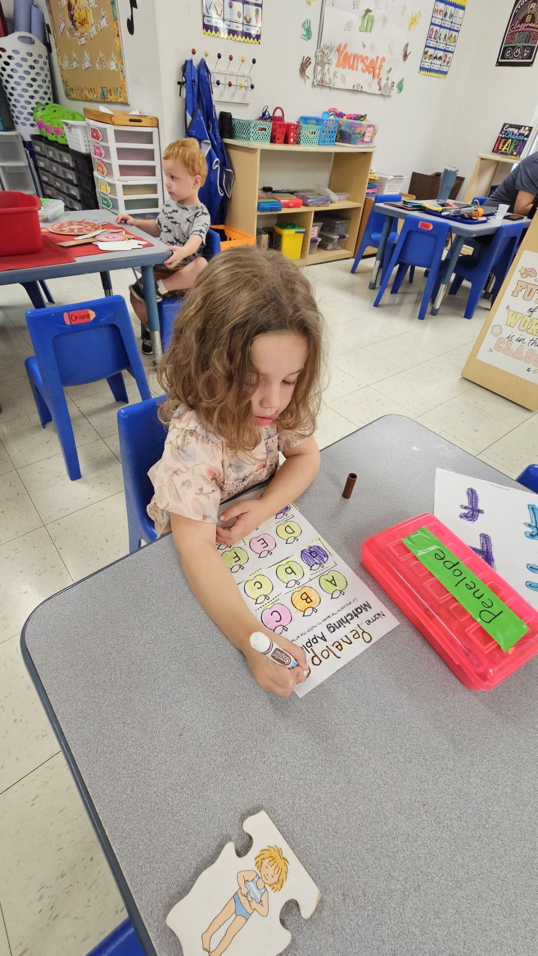 A preschool girl matching letters on a worksheet in a Montessori classroom