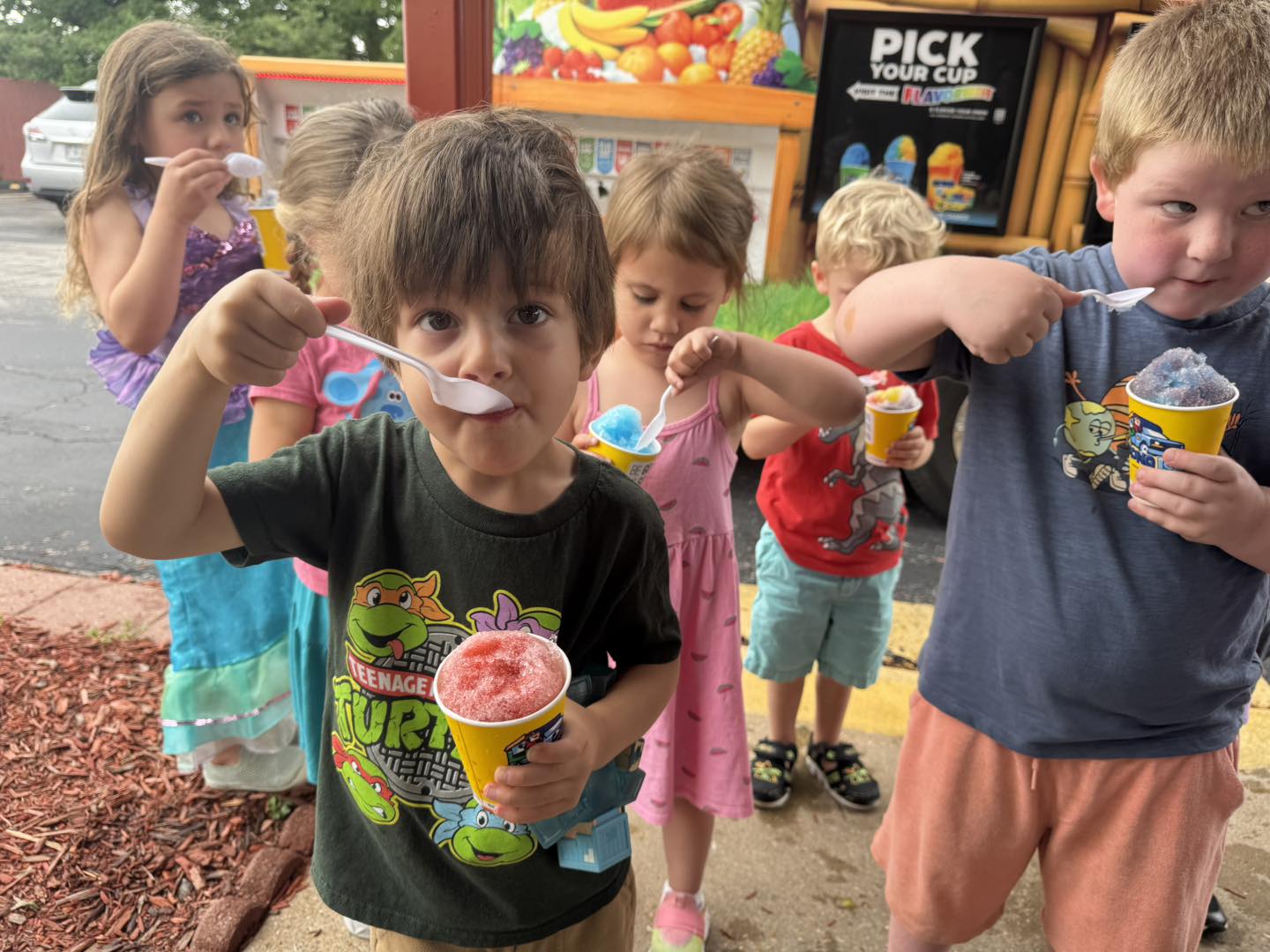 Preschoolers outside sharing shaved-ice cups on a summer afternoon