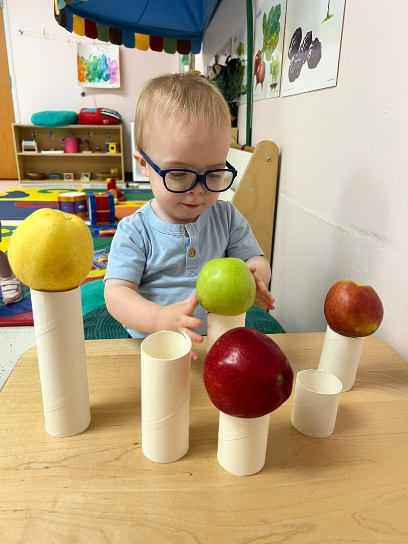 A toddler balancing apples on paper tubes