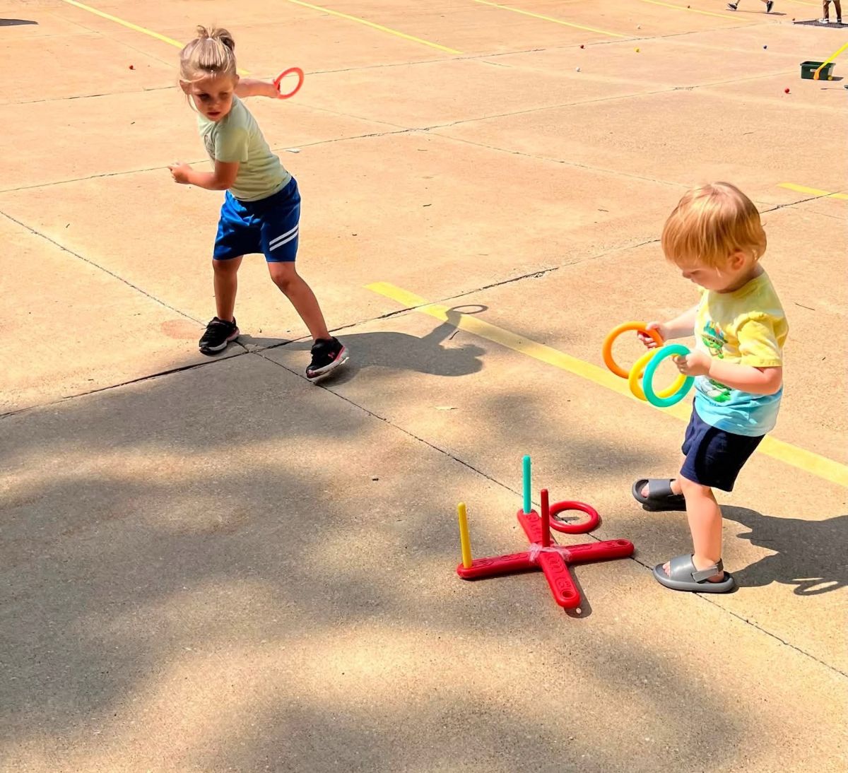 Two children playing ring toss on a sunny outdoor play pad