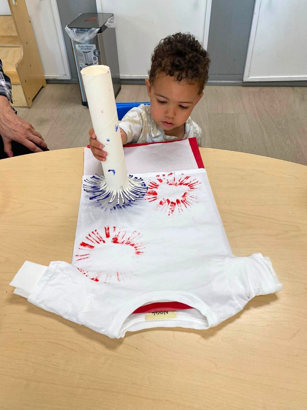 A toddler printing red and blue starbursts on a t-shirt with a paper tube