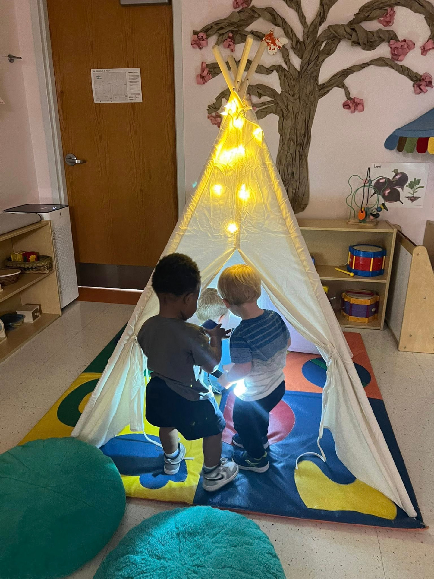 Two toddlers exploring a lit canvas tent in the classroom